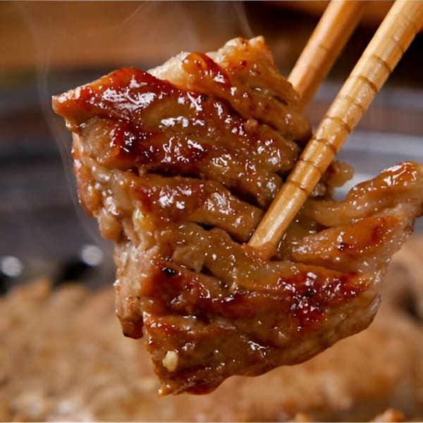 Chopsticks holding up a piece of glistening, grilled Macheko Korean BBQ meat.